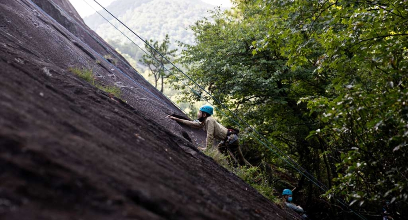 A person wearing safety gear is secured by ropes as they climb up a rock incline.